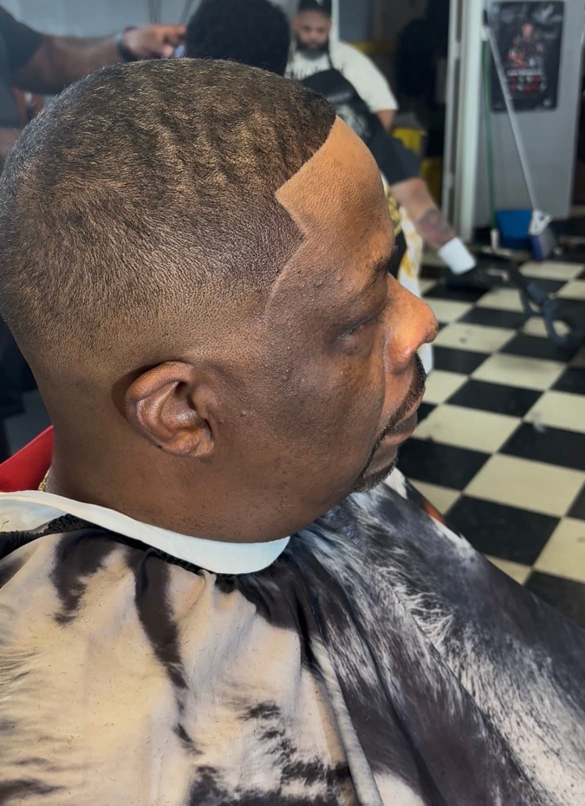 Side profile of a man with a fresh fade and sharp hairline in a barbershop.