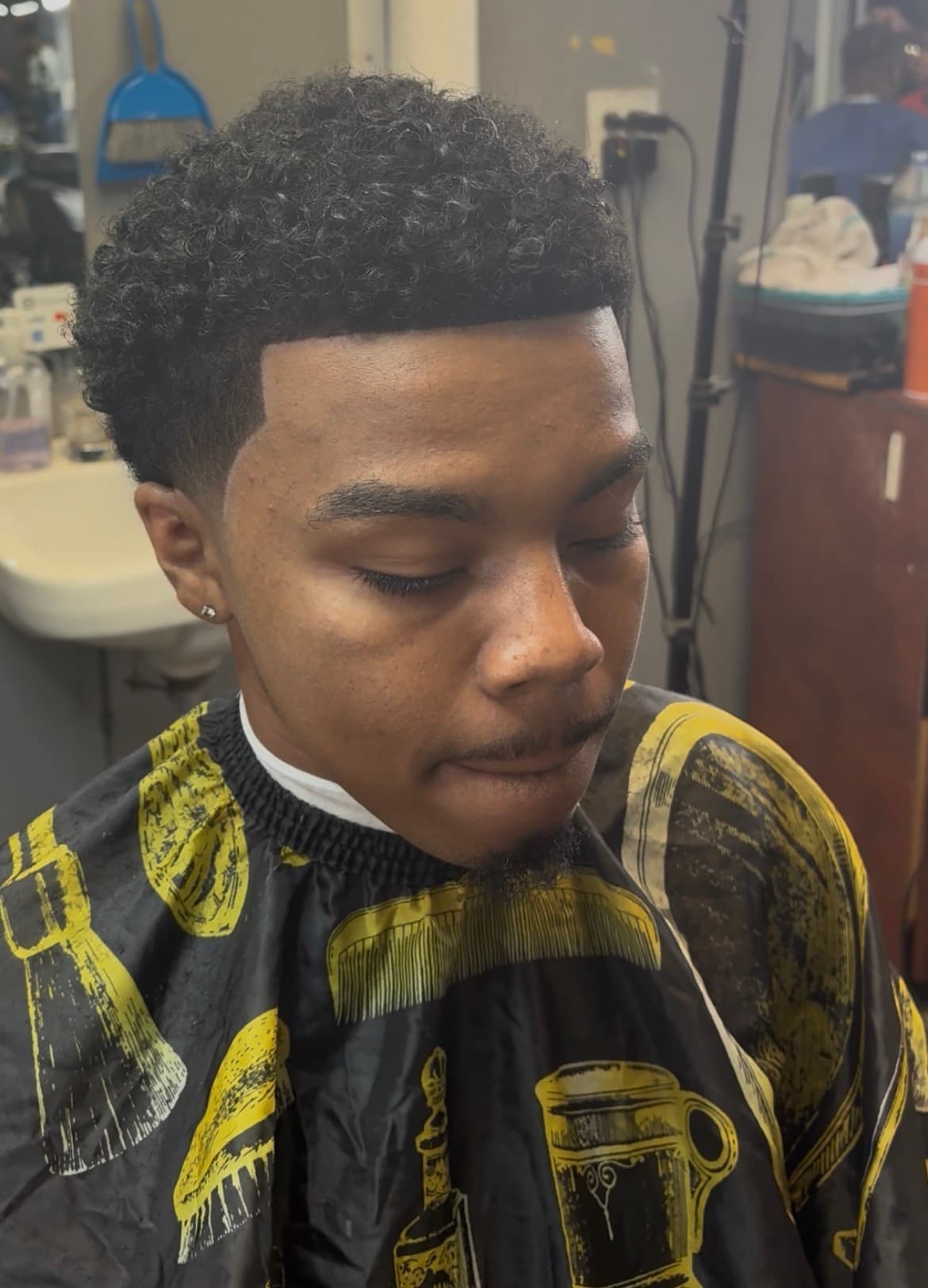 Young man with fresh curly taper fade and sharp hairline wearing a black barber cape.