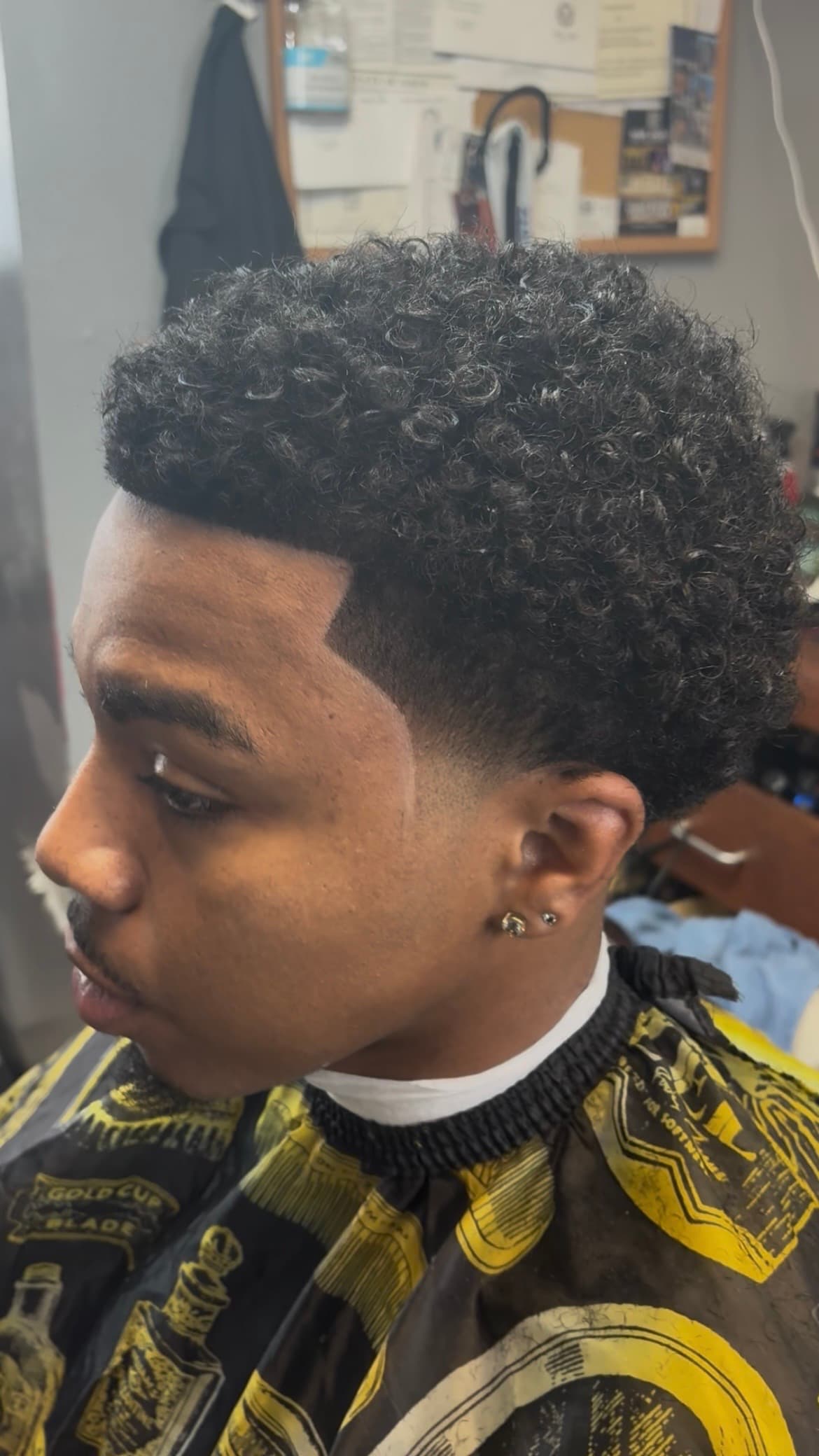 A man with a fresh taper fade haircut, sharp line-up, and natural curly hair.