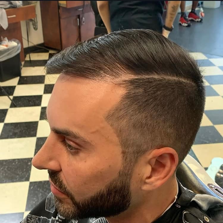 Side profile of a man with a slicked-back side part, skin fade, and groomed beard.