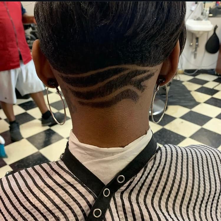 Short dark haircut with decorative wavy shaved patterns at the nape, seen from the back.