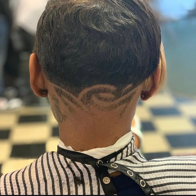 Short dark haircut featuring an intricate swirling design shaved into the nape.