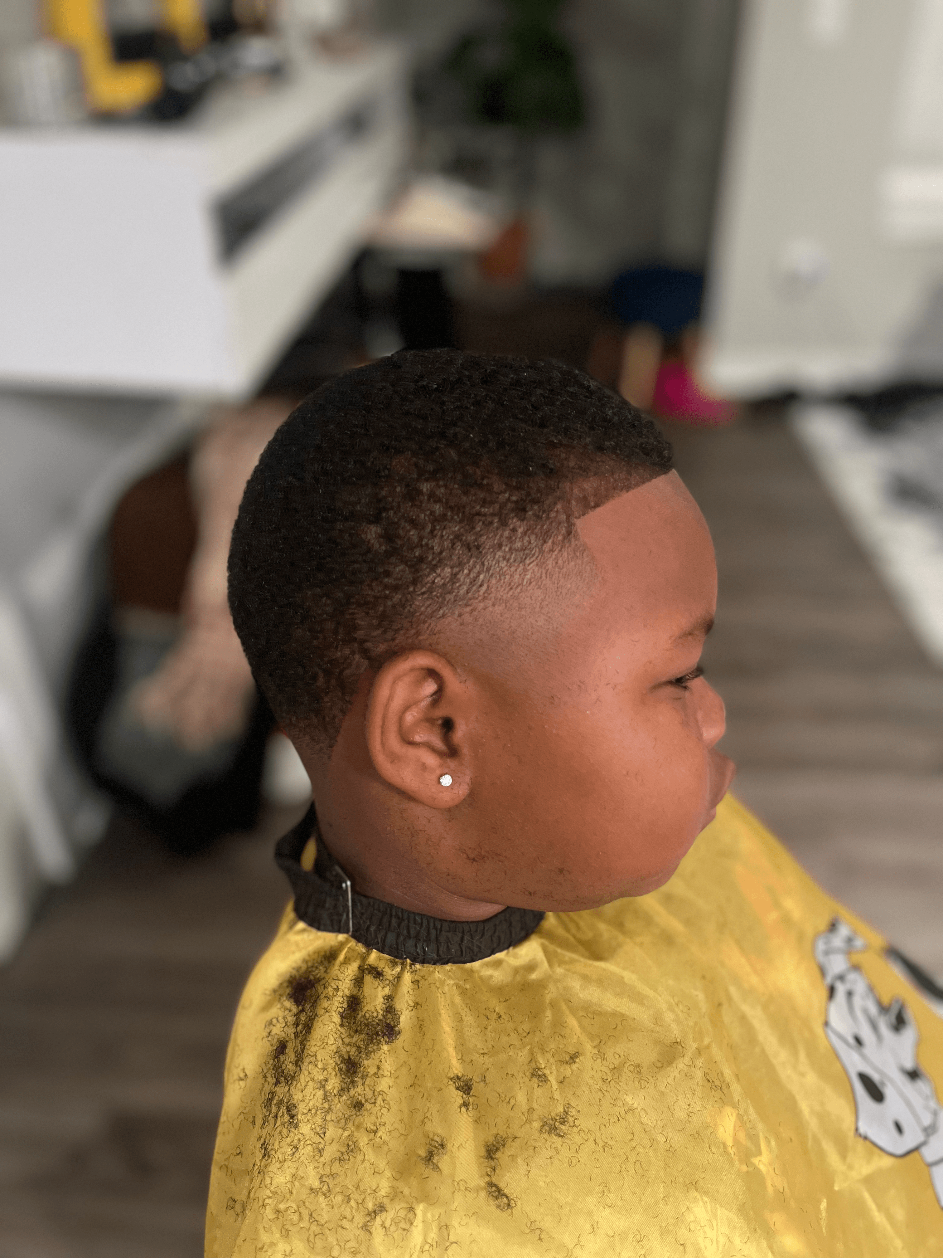 Side profile of a boy with a fresh fade haircut and yellow barber cape.